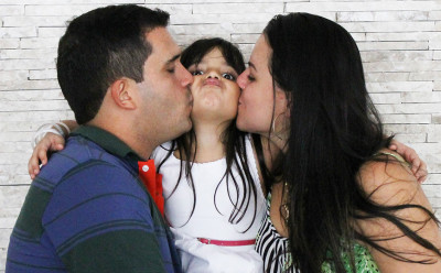 mom and dad kissing daughter on cheek