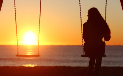 Woman, alone on a swing at sunset