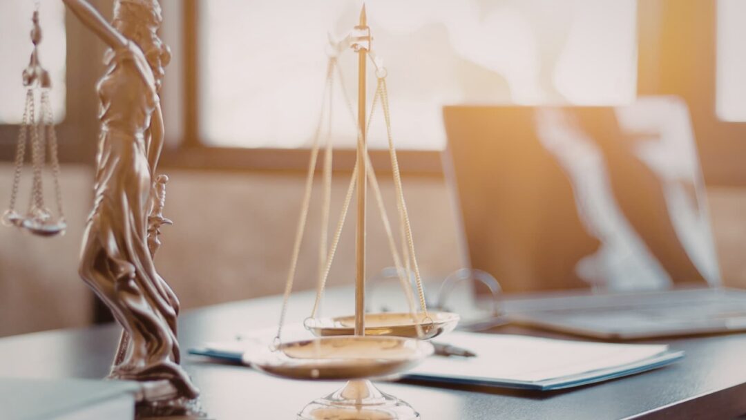 Lady Justice on a desk by a scale on a desk near laptop