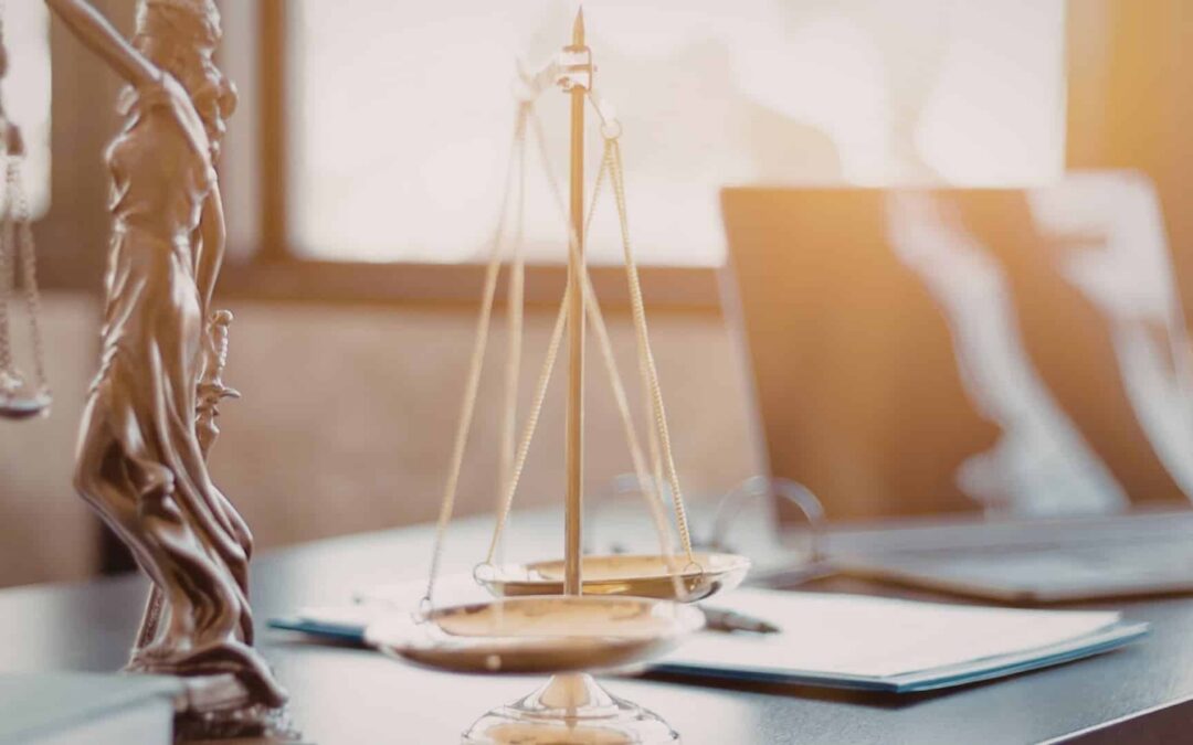 Lady Justice on a desk by a scale on a desk near laptop